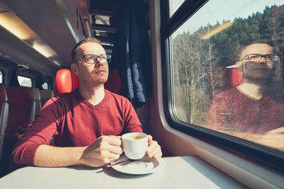 Young man with coffee cup traveling in train