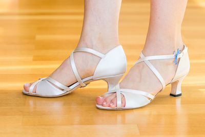 Low section of woman wearing shoes on hardwood floor
