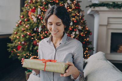 Smiling woman holding gift box against christmas tree