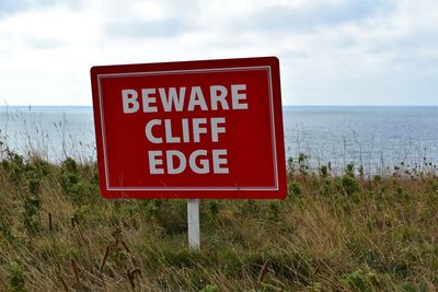 Information sign on grass by sea against sky