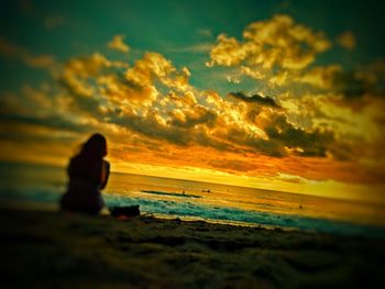 Silhouette woman sitting on beach against sky during sunset