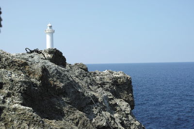 Lighthouse on cliff by sea against clear sky