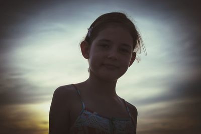 Low angle portrait of girl against cloudy sky during sunset