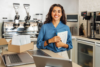 Portrait of smiling young woman standing at coffee shop