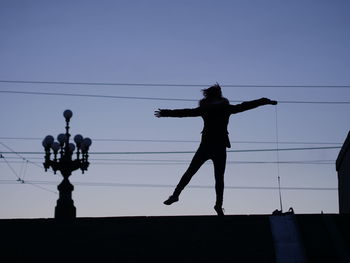 Low angle view of silhouette woman with arms outstretched jumping on field against sky