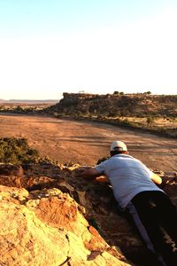 Rear view of man sitting on rock against sky