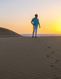 Full length of man standing at beach against clear sky during sunset