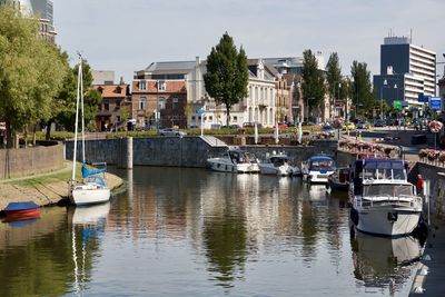 Sailboats moored on river by buildings in city against sky