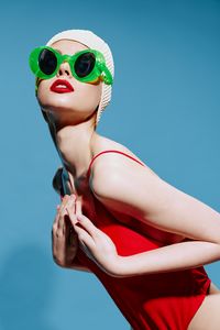 Portrait of young woman wearing sunglasses against blue background