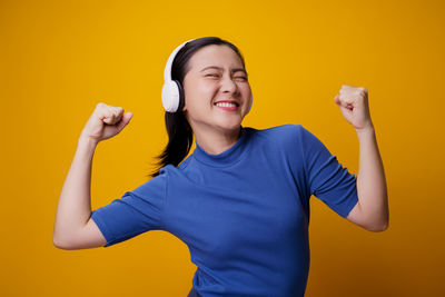 Smiling young woman standing against yellow background