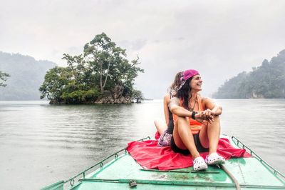 Woman sitting on boat against lake against sky