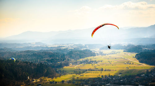 Person paragliding over landscape against sky