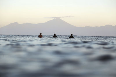 People on sea by mountains against sky