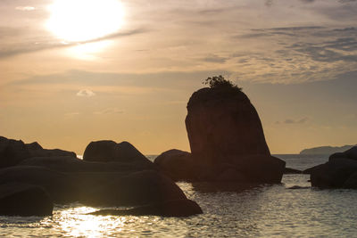 Silhouette rock by sea against sky during sunset