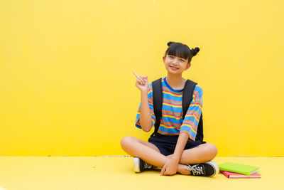 Portrait of a smiling young woman sitting against yellow wall