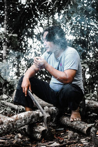 Full length of man sitting by tree in forest