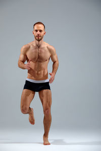 Shirtless young man exercising against white background