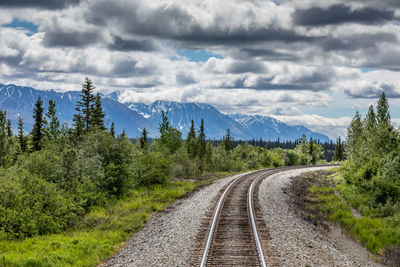 Empty railroad tracks amidst trees in forest against cloudy sky