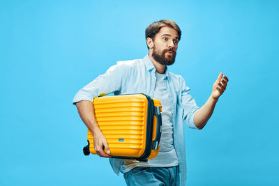 Young man holding suitcase against colored background