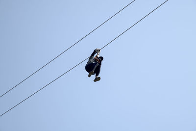 Low angle view of woman zip lining against clear sky