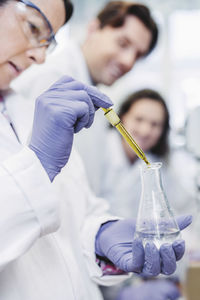 Female scientist analyzing medical sample at laboratory with colleagues in background