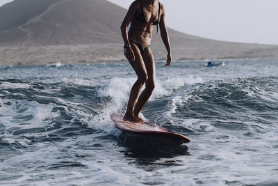 Lower part of female surfer in bikini surfing in sea