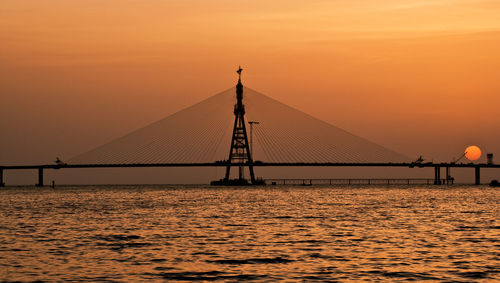 Silhouette suspension bridge over sea against sky during sunset
