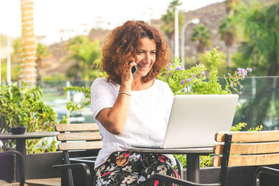 Woman using laptop and mobile phone while sitting on table in cafe