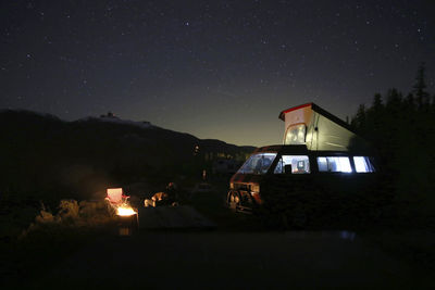 Person sitting by motor home at campsite against sky