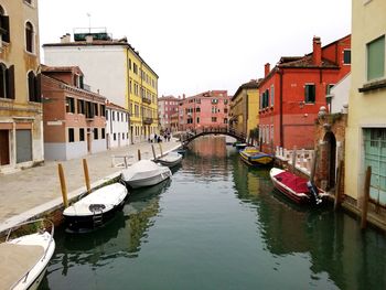 Boats moored in canal amidst buildings against sky