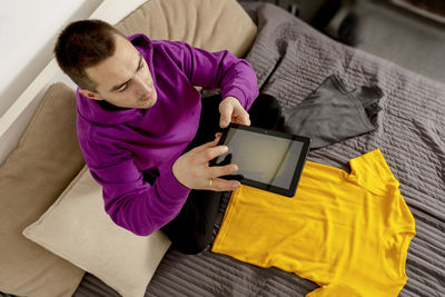 Man with violet hoodie using digital tablet, takes a photo of his old clothes to sell them online