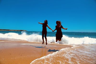 Portrait of smiling friends jumping at beach