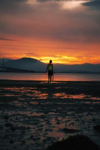 Man standing on beach against sky during sunset
