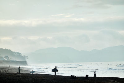 Silhouette people on beach against sky in foggy morning