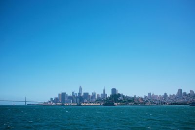 Sea and buildings in city against clear blue sky