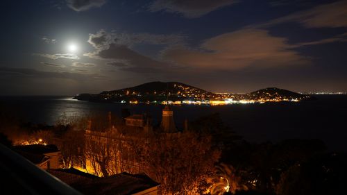 Illuminated city by sea against sky at night