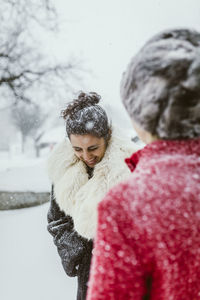 Cheerful female friends standing on field during snowfall