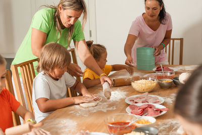 Mothers assisting kids preparing food at kitchen