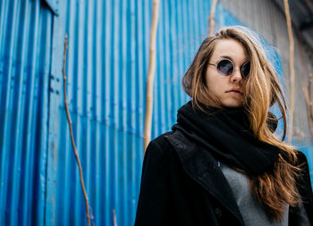 Portrait of young woman wearing warm clothing against corrugated iron