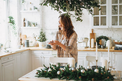 Attractive curly hair woman in plaid shirt takes photo gift box on festive table with fir 