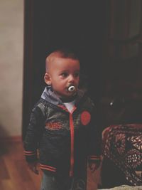 Thoughtful baby boy with pacifier standing at home