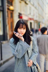 Portrait of young woman holding mobile phone while standing outdoors