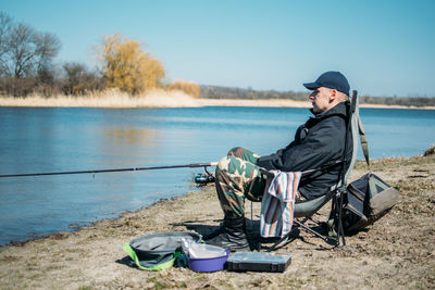 Man sitting by lake against sky