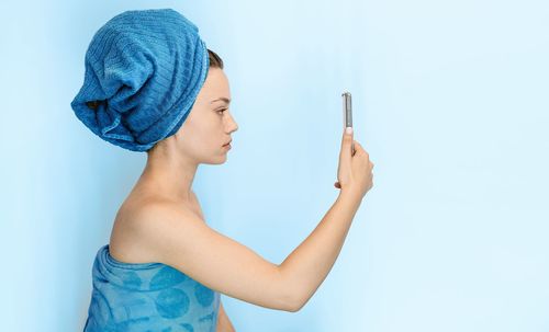 Midsection of young woman holding smart phone against blue background