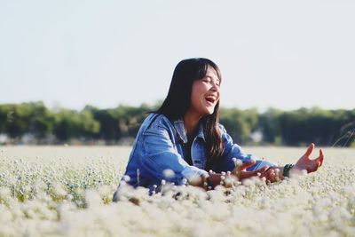 Happy teenage girl amidst flowering plants on field against clear sky