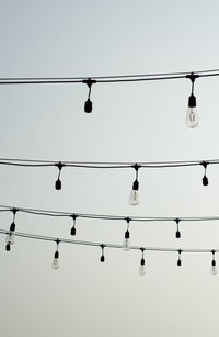 Low angle view of light bulbs hanging against clear sky