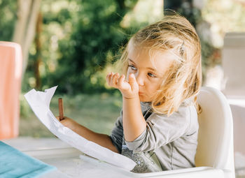 Cute girl holding paper while sitting on seat