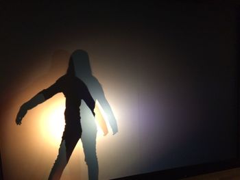 Silhouette man standing by illuminated lamp against sky during sunset