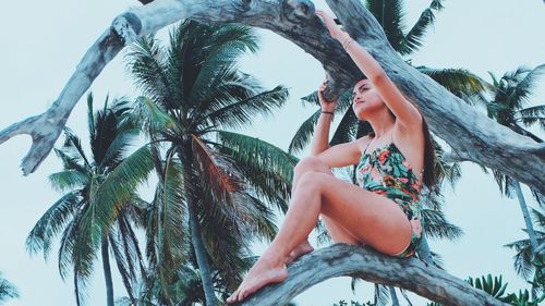 Low angle view of young woman against palm tree