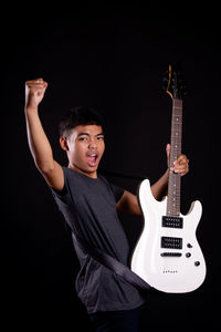 Portrait of a boy playing guitar against black background